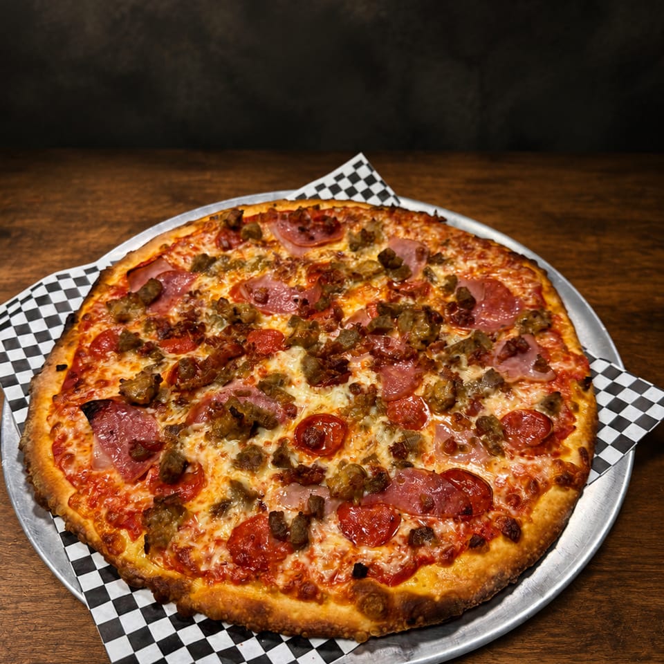 A large, hot meat lover's pizza with pepperoni, sausage, and ham on a metal pan.