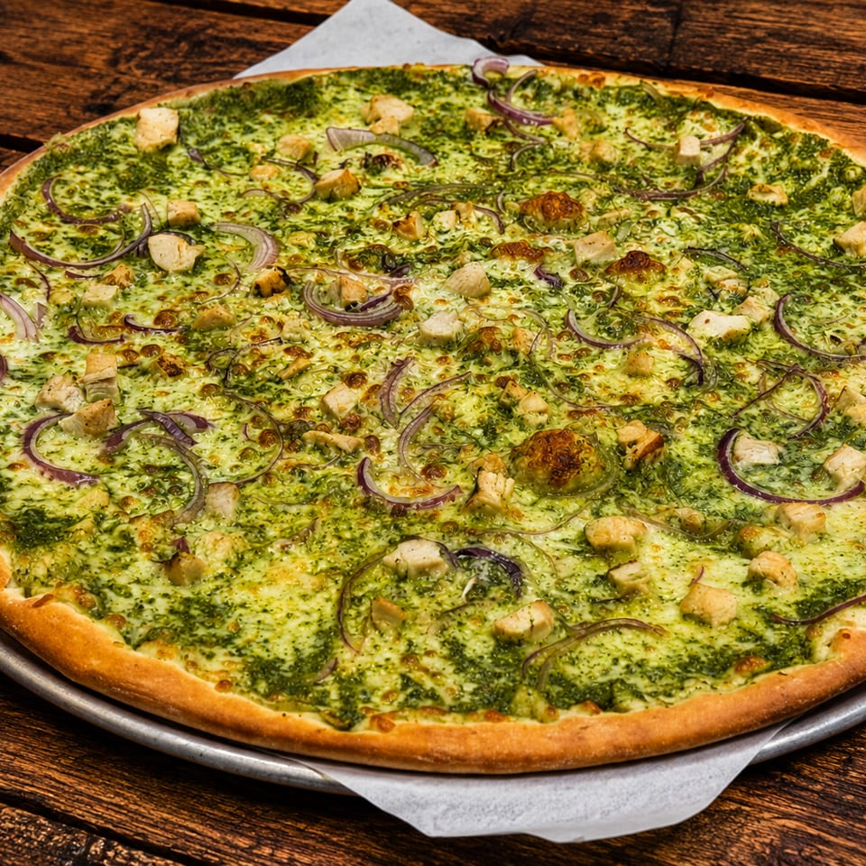 Large pesto chicken pizza with red onions on a wooden table.